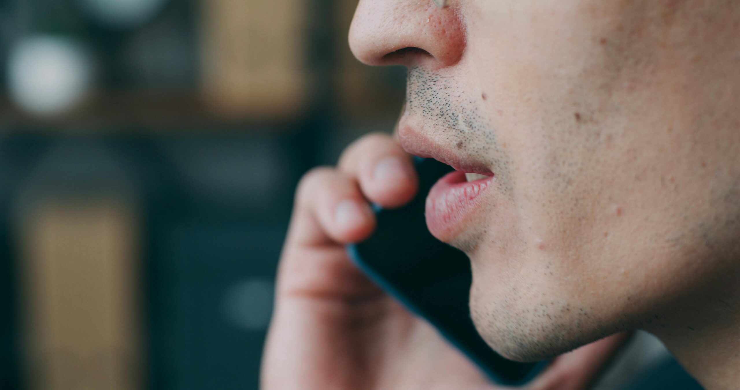 Side profile of an adult speaking on a smartphone indoors.